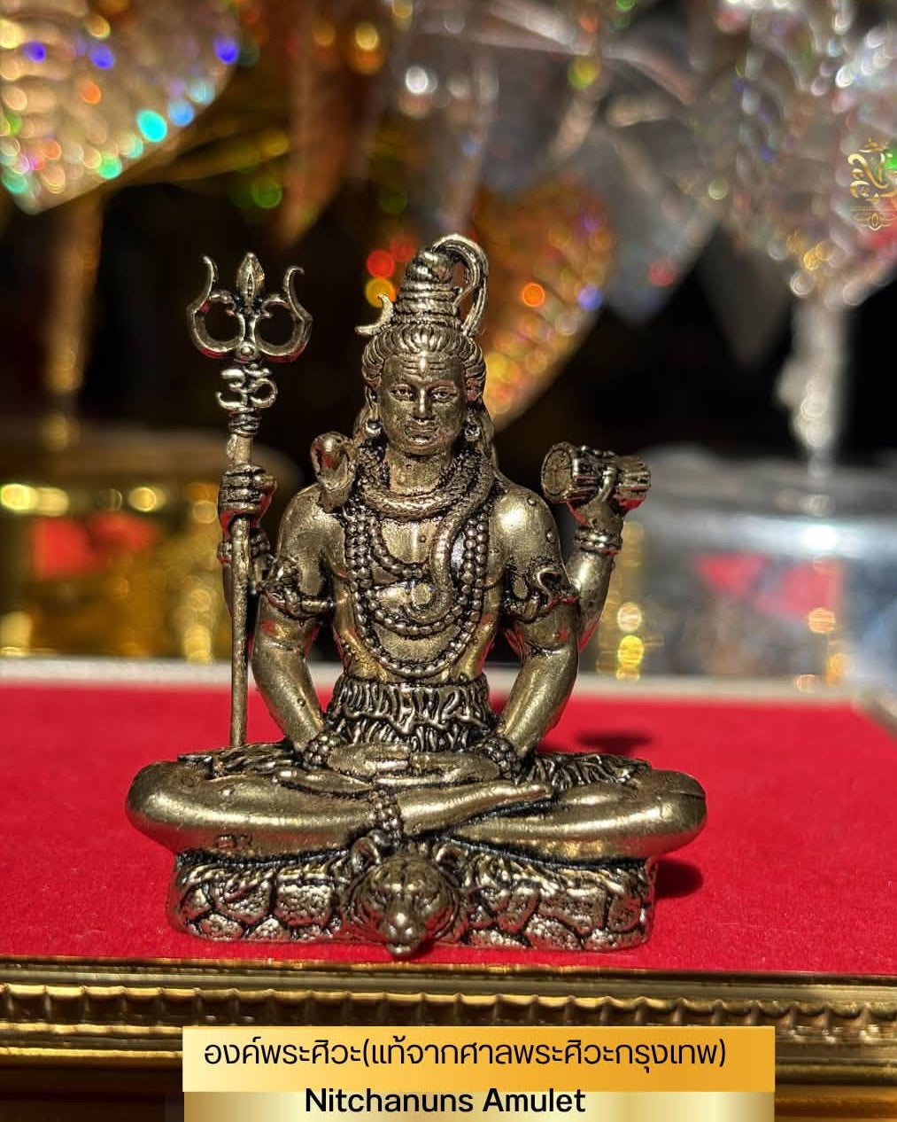 A small metallic Nithanus Amulet statue of Lord Shiva in a seated position, holding a trident, displayed on a red velvet surface with a gold frame. The image includes a price overlay showing '£55' and a Thai text label at the bottom.